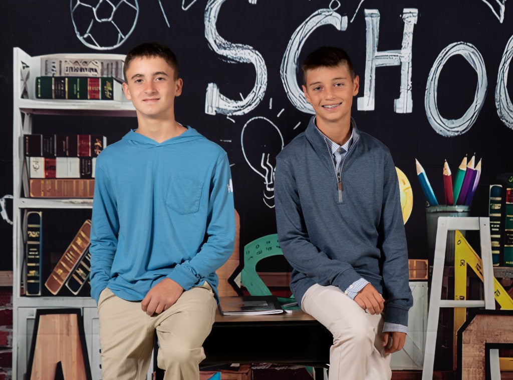 Two boys sitting in from of a chalkboard that reads back to school