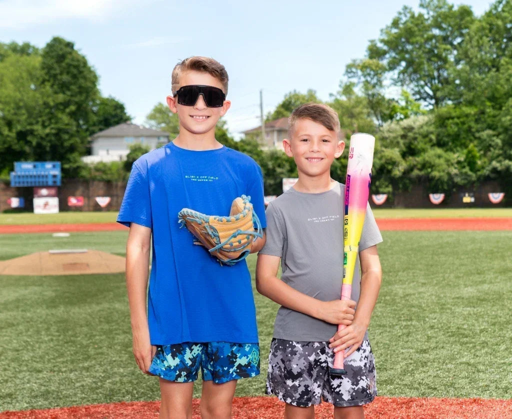 2 boys, one with baseball bat and one with baseball mitt. Wearing athletic t-shirts and camo shorts.