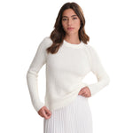 A woman modeling a chalk-colored, long-sleeve ribbed knit sweater against a solid white background.