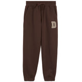A pair of dark brown sweatpants with an elastic drawstring waist and side pockets, featuring a beige block letter 'D' on the left thigh, shown against a plain white background.