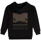 A black pullover hoodie with a rectangular graphic print on the chest. The graphic features a dark brown gradient background with a black silhouette of a city skyline, palm trees, and a grid pattern, with the text 'THE DRIP SHOP • EST. 2023