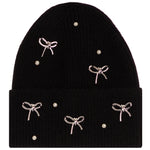 A black ribbed knit beanie hat decorated with five silver bow charms and five small white pearl-like beads, shown against a plain white background.