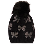 A black knit beanie hat featuring a large black faux fur pom-pom on top and silver rhinestone bow patterns knitted all over the front, shown against a plain white background.