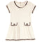 An off-white textured tweed dress with black and white fringed trim, featuring short sleeves, a round neckline, and two decorative patch pockets with button details.