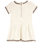 An off-white short-sleeve dress with a textured floral jacquard pattern, featuring dark brown and gold sequined trim along the neckline, sleeve cuffs, and hem, and a central gold zipper.