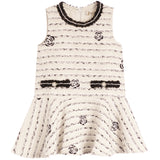 A sleeveless cream-colored tweed dress with black embroidered details, including horizontal stripes, rose motifs, and a decorative waistband.