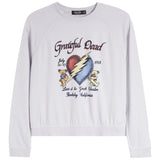 A white long-sleeve crewneck sweatshirt featuring a colorful graphic print on the front. The graphic is inspired by the Grateful Dead, showing a cracked red and blue heart with a yellow lightning bolt, two teddy bears, and text reading 'Grateful Dead', 'July 15-71', '1988', and 'Live at the Great Bear Lake, Berkeley, California'.