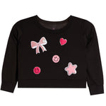 A black long-sleeve sweatshirt for toddlers, featuring pink and white applique patches including a bow, hearts, smiley faces, and a star on the front.