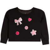 A black long-sleeve sweatshirt for toddlers, featuring pink and white applique patches including a bow, hearts, smiley faces, and a star on the front.