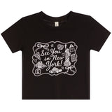 A black short-sleeve crewneck t-shirt with a white graphic print on the front that reads 'See You in New York!' surrounded by New York-themed illustrations like the Statue of Liberty, a cab, and a pizza slice.