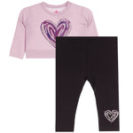A toddler girl's two-piece outfit set featuring a light pink long-sleeve top with a purple glitter heart graphic on the front, paired with black leggings that have a small white glitter heart on the lower leg.