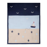 A square navy blue blanket or throw featuring a nautical design with a light blue sky, beige sand, a small sailboat, seagulls, anchors, and starfish.