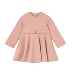 A pink long-sleeve baby dress with a subtle polka dot pattern, featuring a gathered waist with a small gold-tone metal accent, displayed on a clean white background.