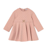 A pink long-sleeve baby dress with a subtle polka dot pattern, featuring a gathered waist with a small gold-tone metal accent, displayed on a clean white background.
