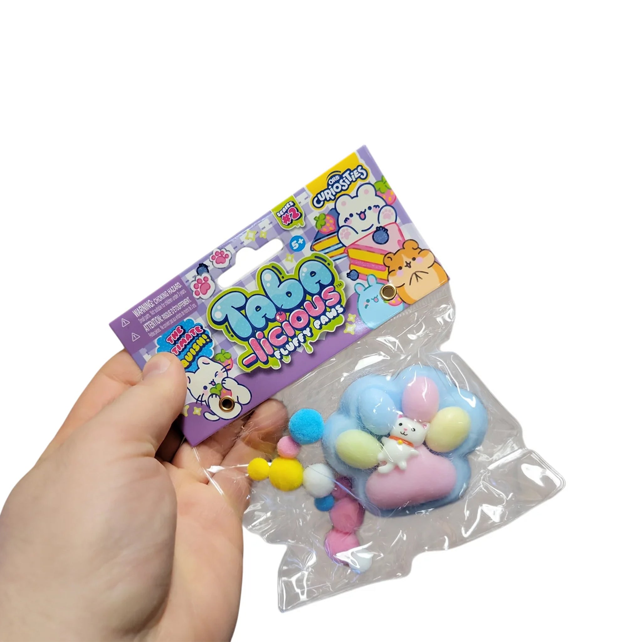 A hand holding a packaged novelty squishy toy. The product is a pastel-colored cloud-shaped squishy with a small white bear character, accompanied by small pastel pom-poms.