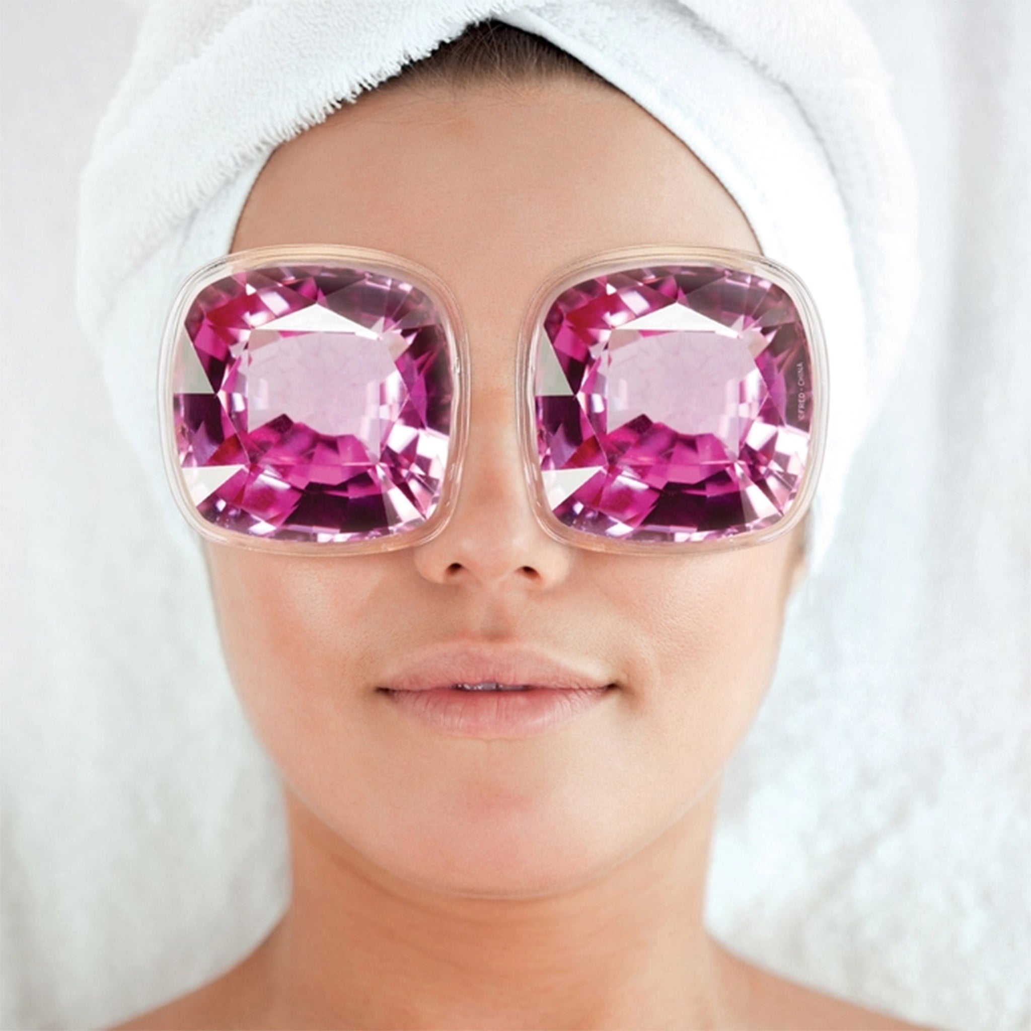 Person wearing eye patches with pink gemstones and a white towel on their head.