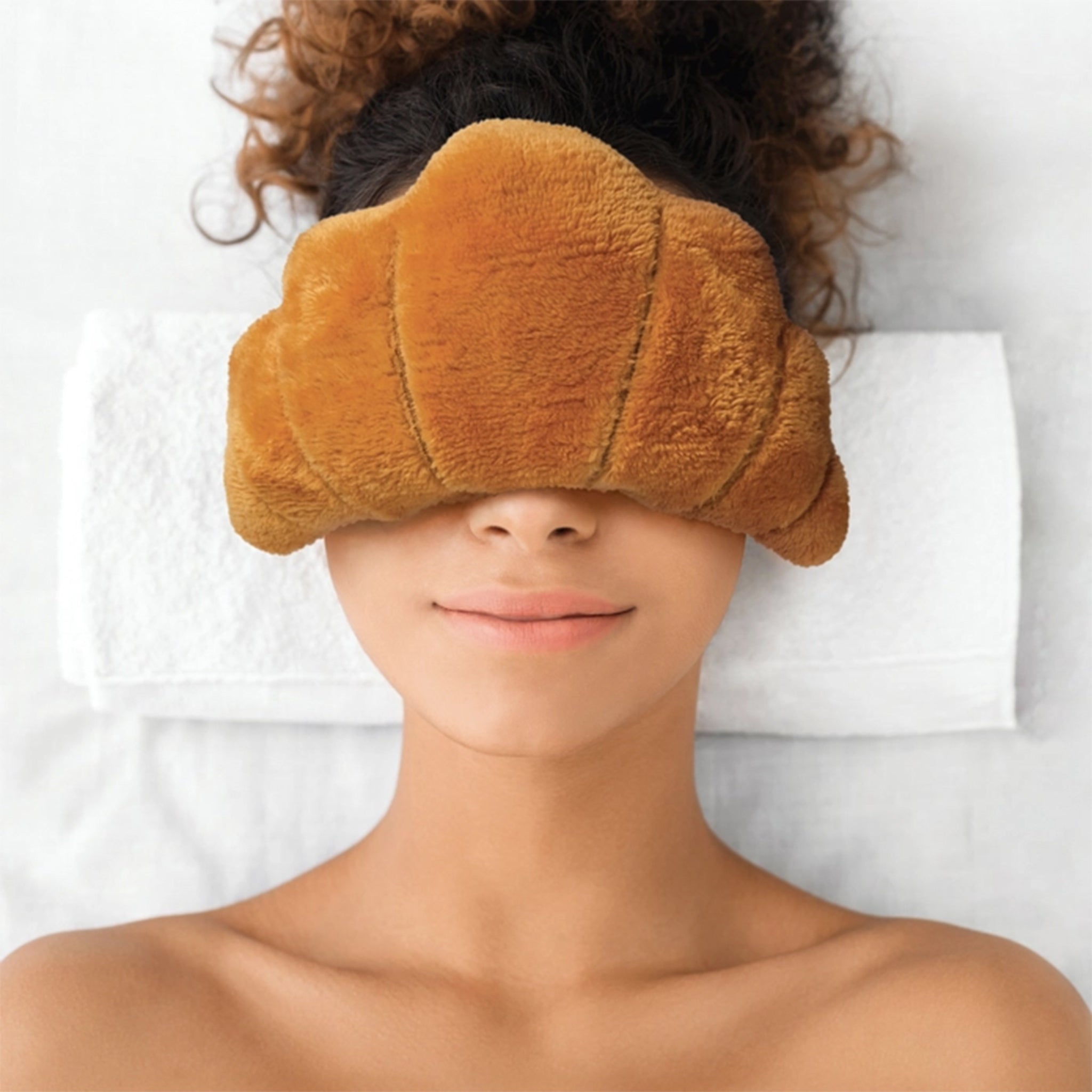 Person wearing a brown plush eye mask on a white background