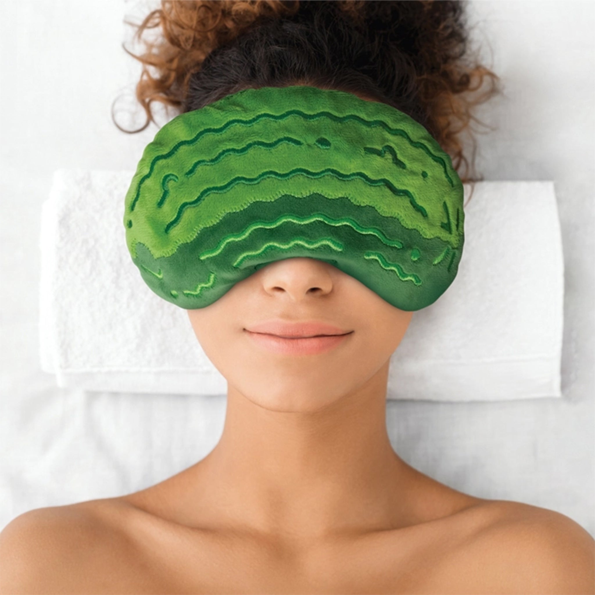 Person wearing a green watermelon-shaped sleep mask on a white background