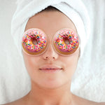 Person wearing donut-shaped eye masks with sprinkles on a plain background