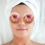 Person wearing donut-shaped eye masks with sprinkles on a plain background