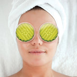 Person wearing pickle slices over their eyes with a towel on their head, against a white background
