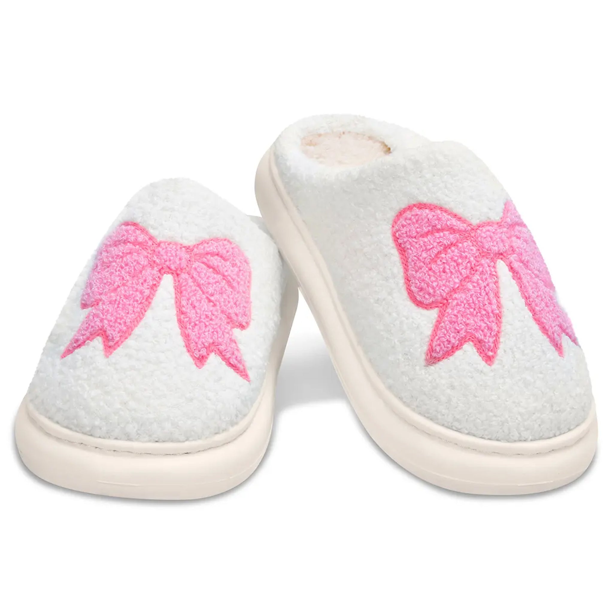 A pair of white fuzzy slip-on slippers with large pink bow designs on the top, shown on a clean white background.