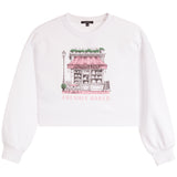 A white cropped sweatshirt with a pink and black line-art graphic of a bakery storefront on the chest, with the words 'FRESHLY BAKED' printed below the illustration.