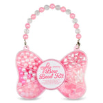 Pink bow-shaped bead kit with a beaded handle, filled with pink and white beads and sequins, on a white background.