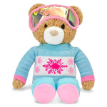 A plush teddy bear wearing a light blue knit sweater with pink and white snowflake patterns, pink goggles, and pink boots, set against a plain white background.
