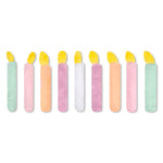 A set of nine plush candle-shaped items in assorted pastel colors with yellow flame tops, arranged in a row on a plain white background.