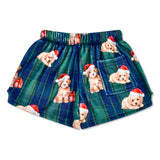 A pair of children's plaid shorts featuring a pattern of small golden puppy illustrations wearing red Santa hats, with a blue pocket on the left leg, set against a plain white background.