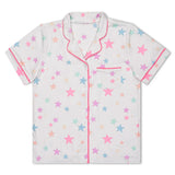 A short-sleeve pajama shirt with a white base, decorated with a pattern of pastel pink, blue, and yellow stars, and finished with pink piping on the collar, placket, and sleeve cuffs.