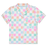 A short-sleeve pajama shirt with a pastel multicolor checkered pattern on a white base, featuring light pink, mint green, and peach squares with small smiley faces, hearts, stars, and a chest pocket.