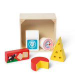 A children's wooden toy cheese set with a natural wood box, including a white block labeled cow, a round labeled milk, a red and yellow cheese wedge, a yellow cheese block, and a red box with a cow illustration.