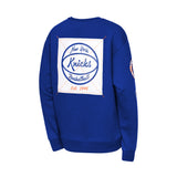 A royal blue crewneck sweatshirt shown from the back, featuring a large white square graphic with the New York Knicks logo in blue and orange, and a smaller logo on the right sleeve.