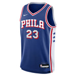 A blue Philadelphia 76ers basketball jersey with 'PHILA' and the number '23' in white with red outlines, featuring a white side panel with three blue stars and a white Nike swoosh on the chest.