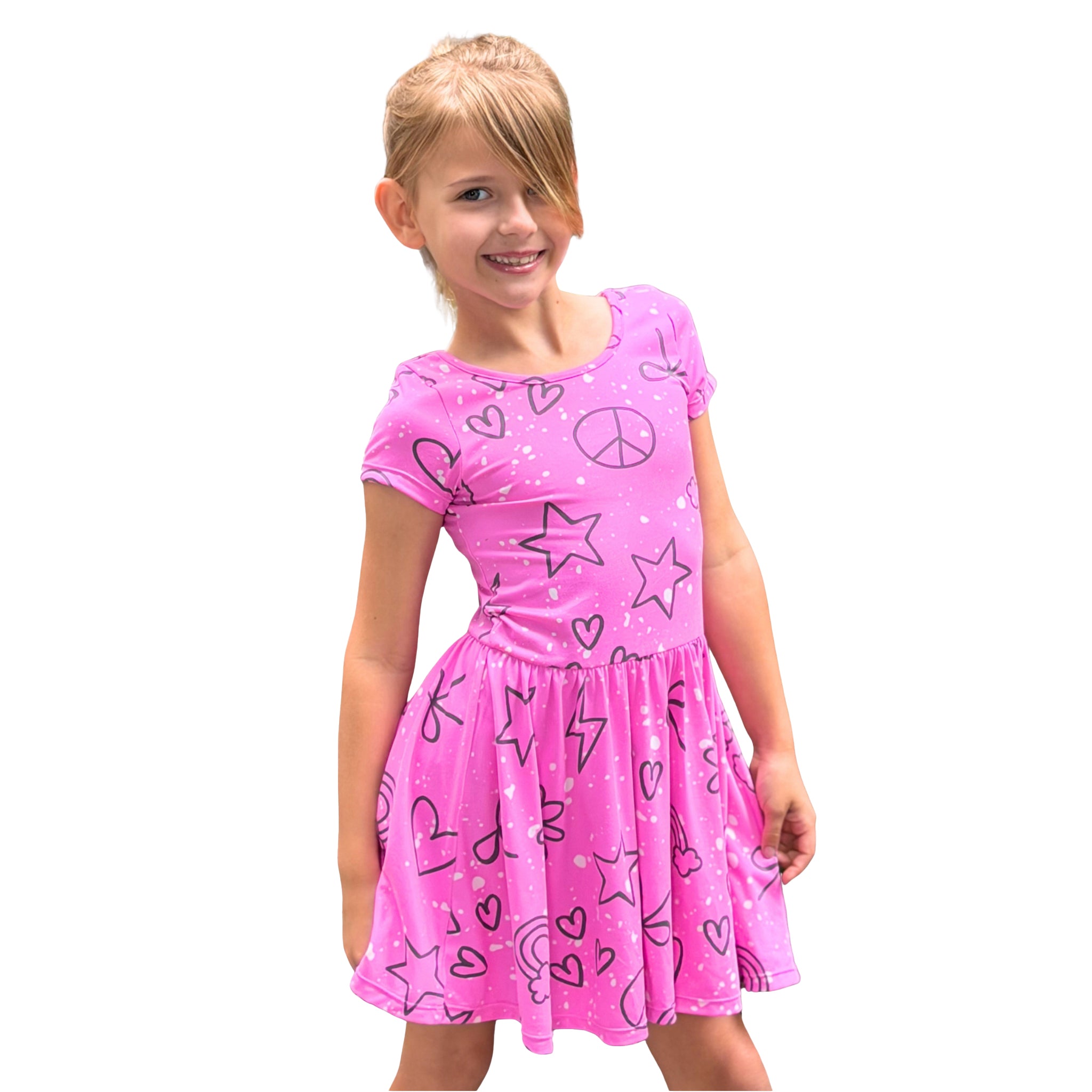 A young girl with blonde hair wearing a bright pink short-sleeve dress with black line-art graphics of stars, hearts, peace signs, and rainbows, set against a plain white background.