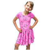 A young girl with blonde hair wearing a pink short-sleeve dress with black peace signs, stars, and hearts, posing with hands on hips against a solid white background.