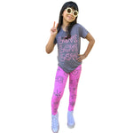 A young girl modeling a gray t-shirt with three 'LOVE' printed in pink, paired with bright pink leggings featuring black rainbow, heart, and bow designs, and white sneakers, against a solid white background.