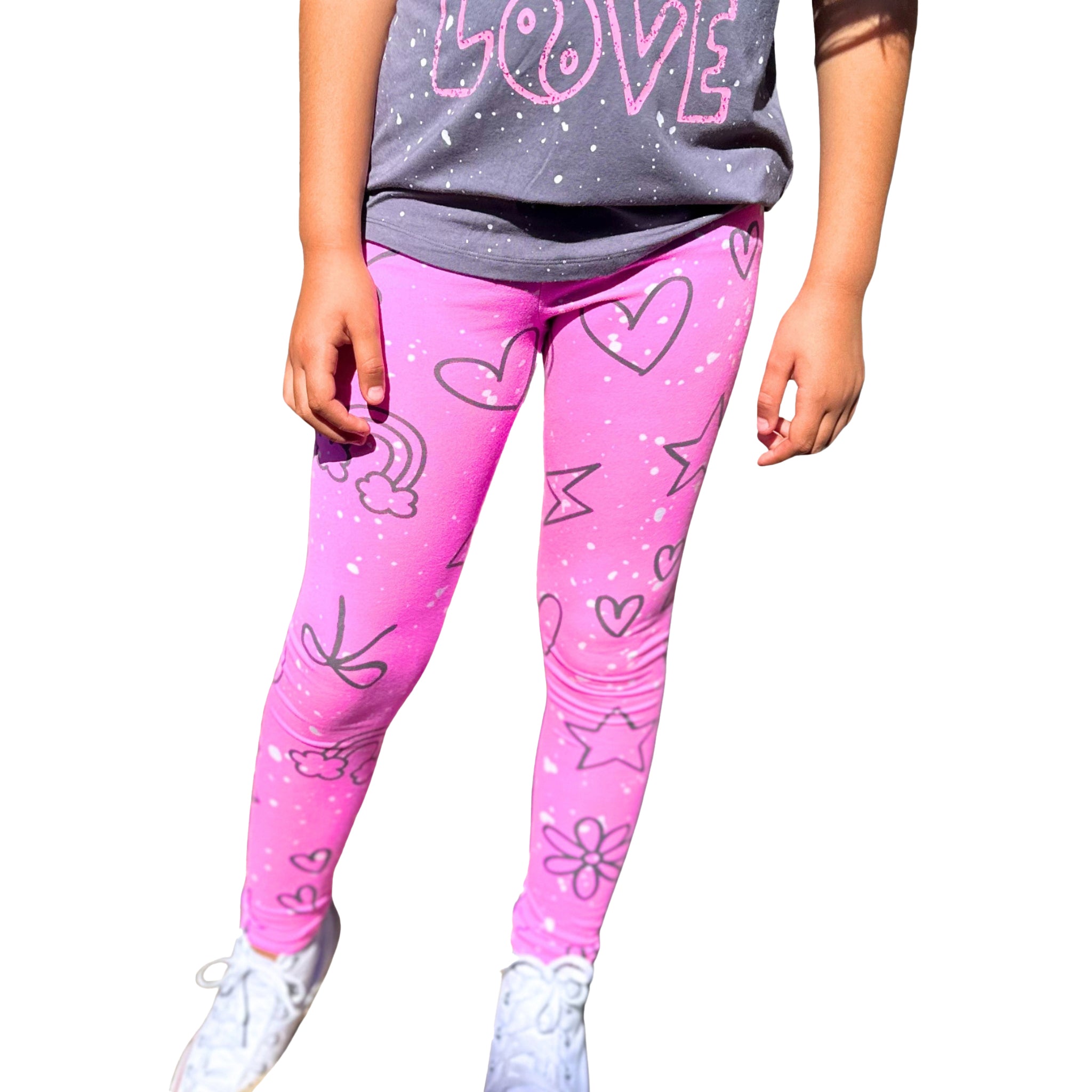 Pink leggings with a white speckled pattern and black heart, star, and flower drawings, worn by a child with a gray t-shirt and white sneakers against a white background.