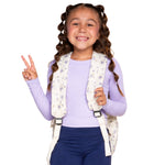 A young girl with bubble braided hair, smiling, and makes a peace sign while wearing a floral-patterned backpack over a light purple long-sleeve shirt and navy pants, set against a solid white background.