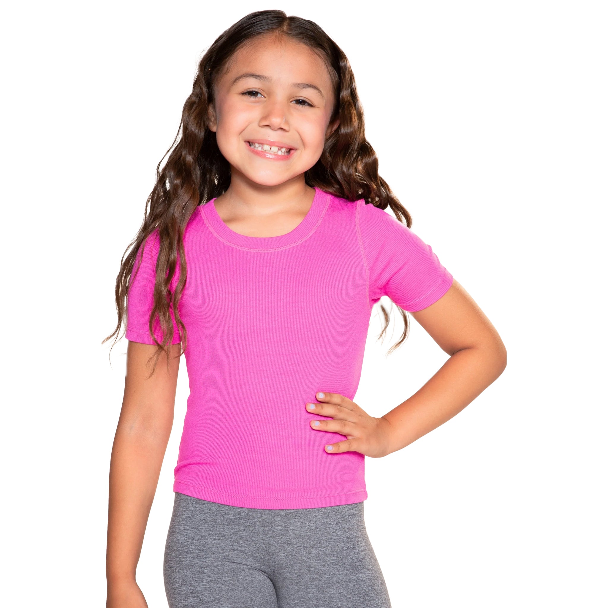 A young girl with long brown hair smiling, wearing a bright pink short-sleeve crewneck athletic t-shirt and gray leggings, posing against a solid white background.