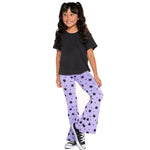 A young girl with long dark curly hair is modeling a two-piece outfit consisting of a plain black short-sleeve t-shirt and light purple flare pants covered in a black star pattern. She is wearing black and white sneakers against a solid white background.