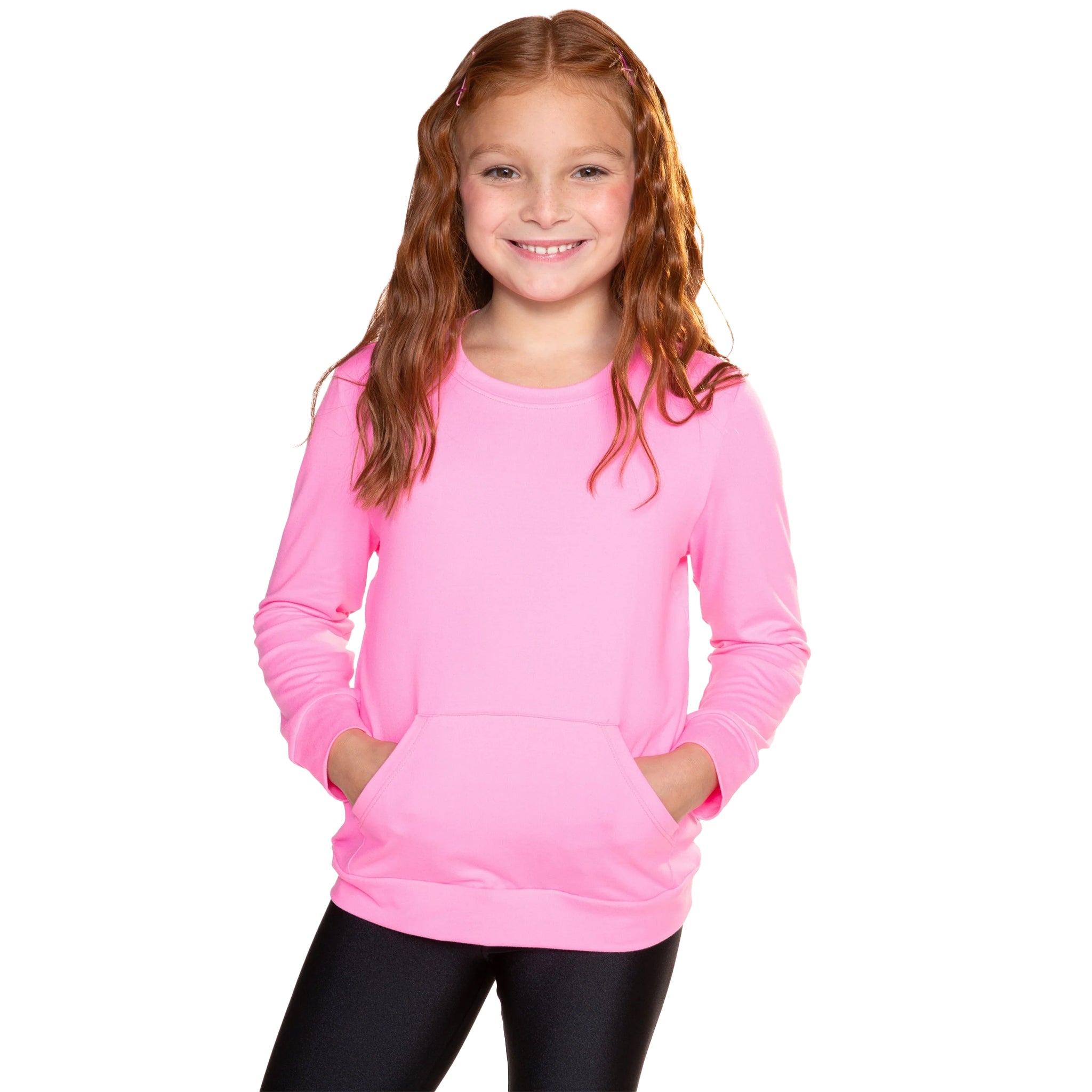 A young girl with long red hair smiling, wearing a bright pink long-sleeve crewneck sweatshirt with a front kangaroo pocket, paired with black leggings, against a solid white background.