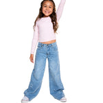 A young girl with long brown hair stands against a white background wearing a light pink long-sleeve crop top and light blue wide-leg denim jeans decorated with white star prints.