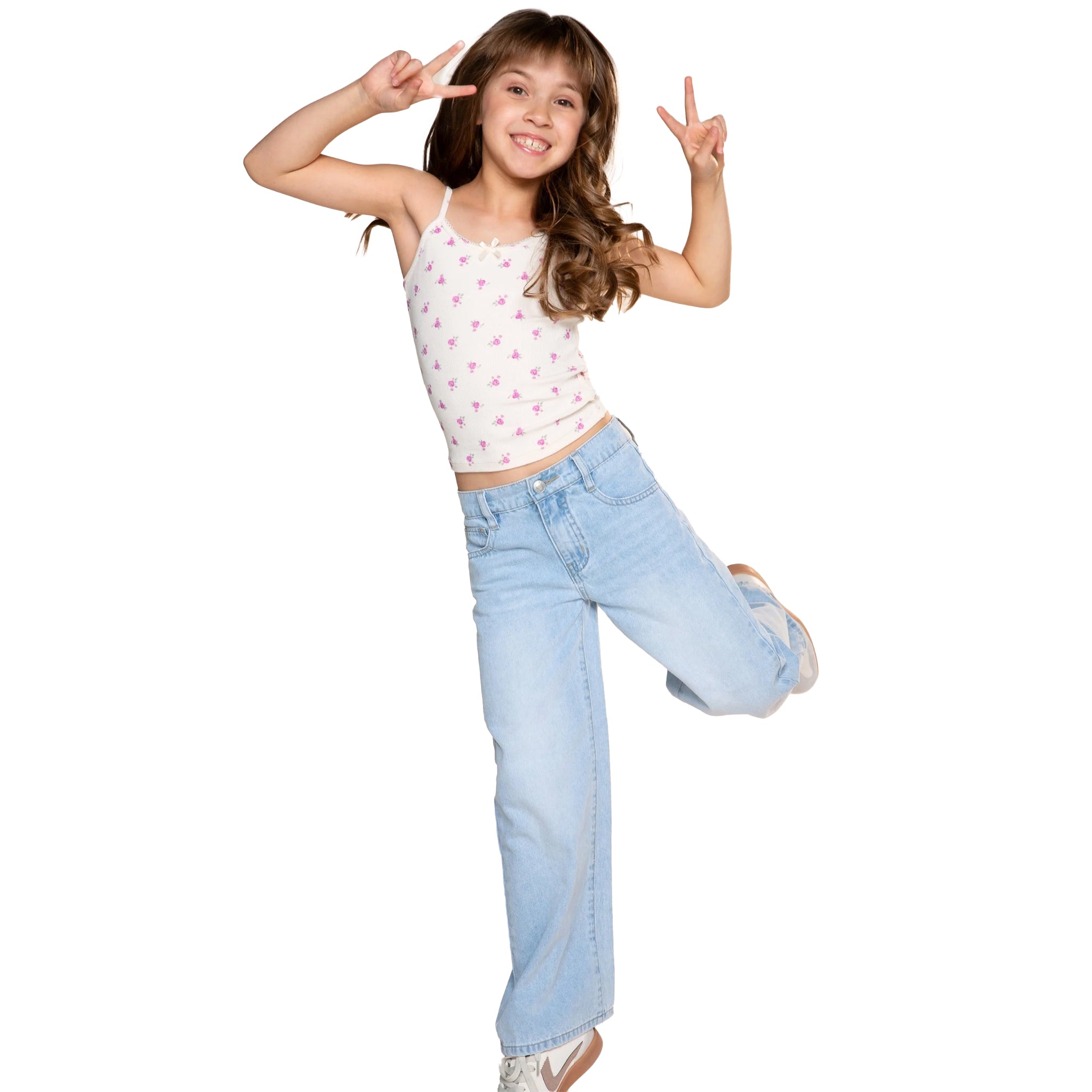 A young girl posing in a white spaghetti-strap crop top with a pink floral pattern and light-wash wide-leg jeans, making peace signs against a solid white background.
