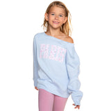 A young girl with blonde hair wearing a light blue off-the-shoulder sweatshirt with 'PARIS' printed in pink and white on the front, paired with pink leggings, against a solid white background.