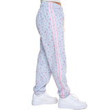 Light blue jogger sweatpants with a pink floral print, featuring a pink stripe down the side and white sneakers shown on a model from the waist down against a white background.