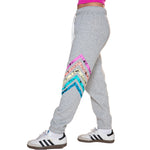 A person wearing heather gray jogger sweatpants with a colorful chevron pattern on the side, paired with white sneakers, shown from the waist down against a plain white background.