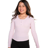 A young girl with long dark hair smiling, wearing a light pink long-sleeve henley shirt with three buttons and black pants, set against a plain white background.